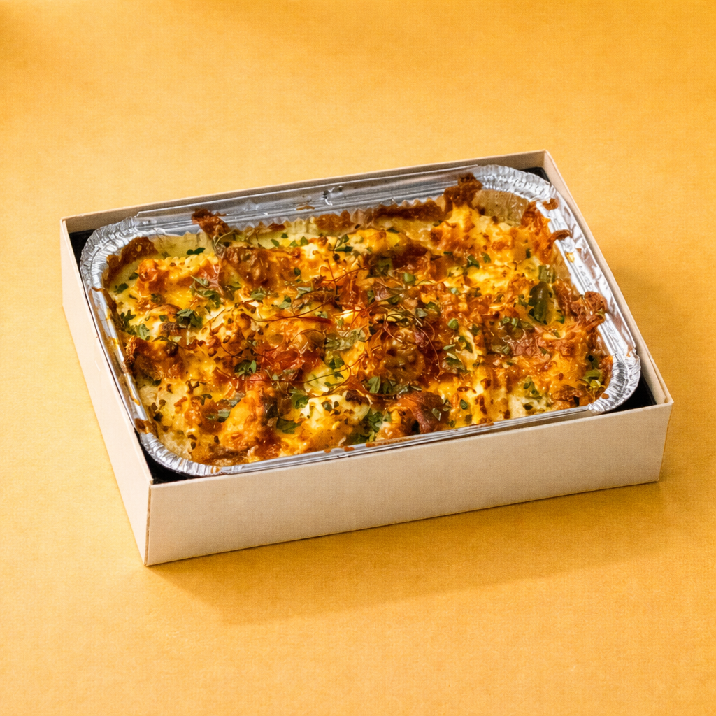Baked dish in a foil tray inside a crate box looking bento box with a yellow background