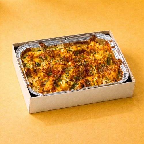 Baked dish in a foil tray inside a crate box looking bento box with a yellow background