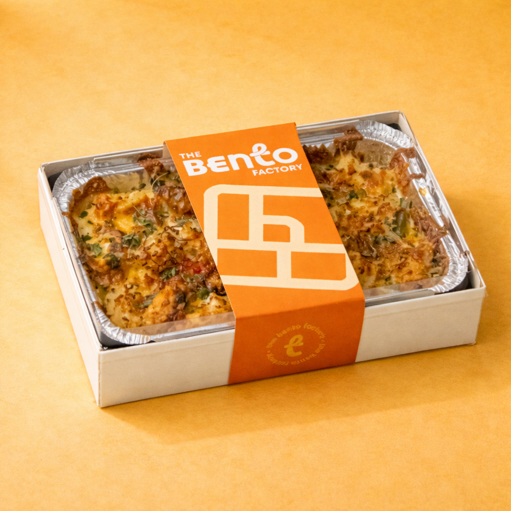 Baked Seafood Pasta in Bento box with 'The Bento Factory' brand sleeve on a yellow background