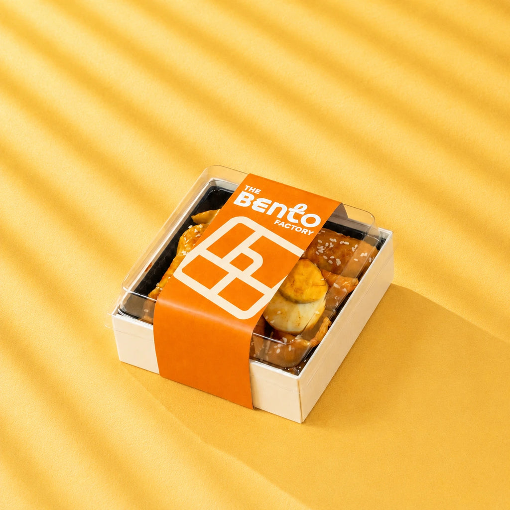 Chewy Korean rice cakes bathed in a rich sweet-spicy sauce, paired with savoury fish cake and hearty egg in a bento box with the bento factory sleeve