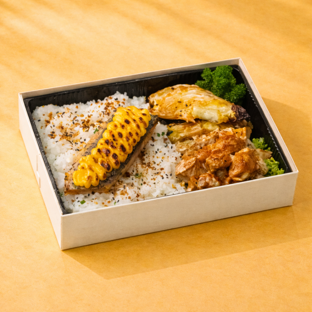 Bento box with mentaiko salmon, potato salad, charred cabba and rice on a yellow background