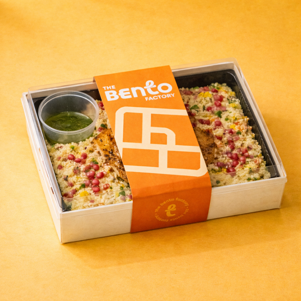 Couscous salad with grilled fish and 'The Bento Factory' packaging on a yellow background