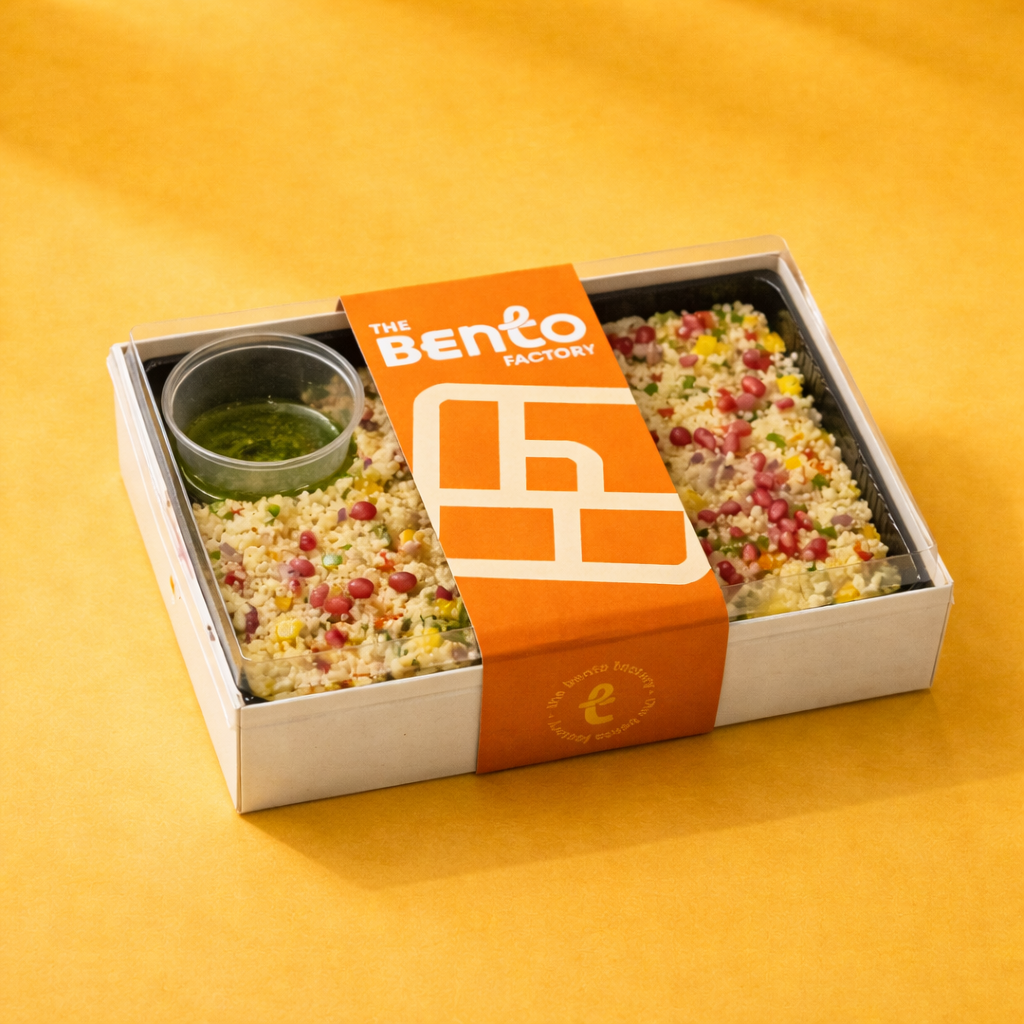 Couscous salad bento box with 'The Bento Factory' branding on a yellow background